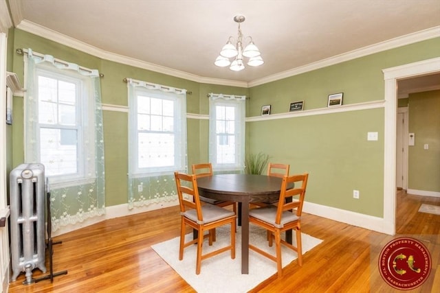 dining area with light wood-style flooring, radiator heating unit, an inviting chandelier, crown molding, and baseboards