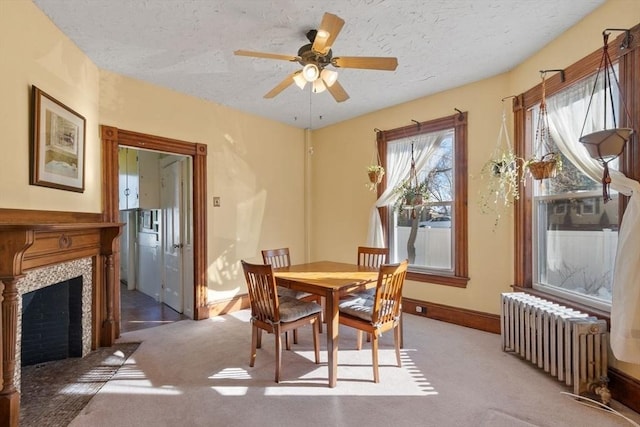 carpeted dining area with a tiled fireplace, ceiling fan, radiator, and a textured ceiling