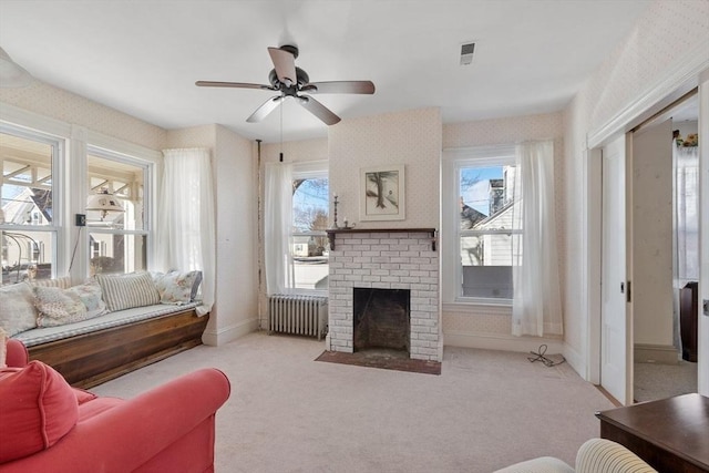 carpeted living room featuring a brick fireplace, radiator heating unit, and ceiling fan