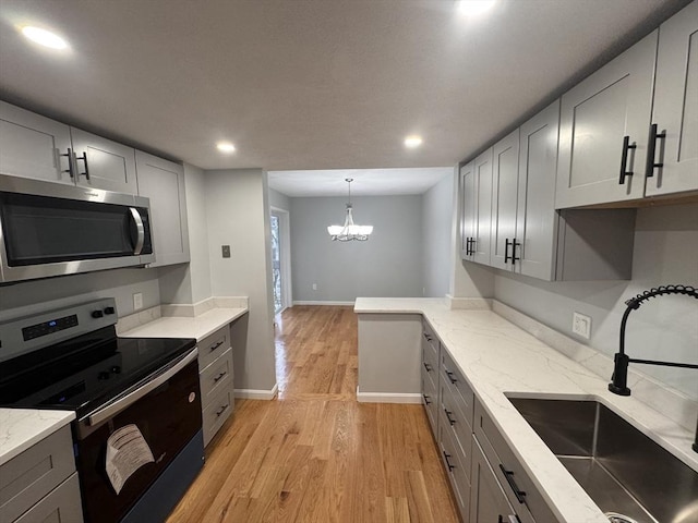 kitchen with gray cabinetry, an inviting chandelier, sink, light hardwood / wood-style flooring, and appliances with stainless steel finishes