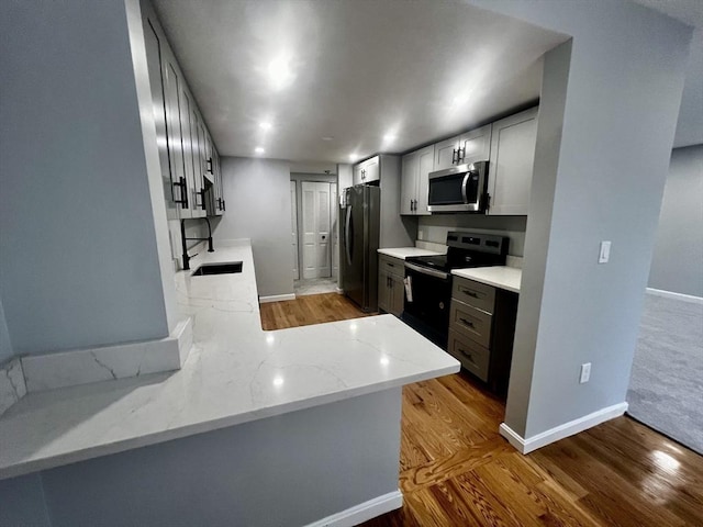 kitchen featuring kitchen peninsula, light stone countertops, hardwood / wood-style floors, and stainless steel appliances