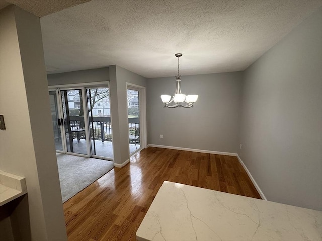 unfurnished dining area featuring hardwood / wood-style floors, a textured ceiling, and an inviting chandelier