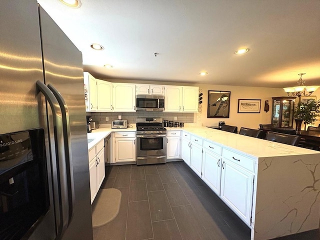 66 Schooner Lndg Unit 66, Hampton, NH 03842 - kitchen featuring appliances with stainless steel finishes, a peninsula, tasteful backsplash, a chandelier, and white cabinets