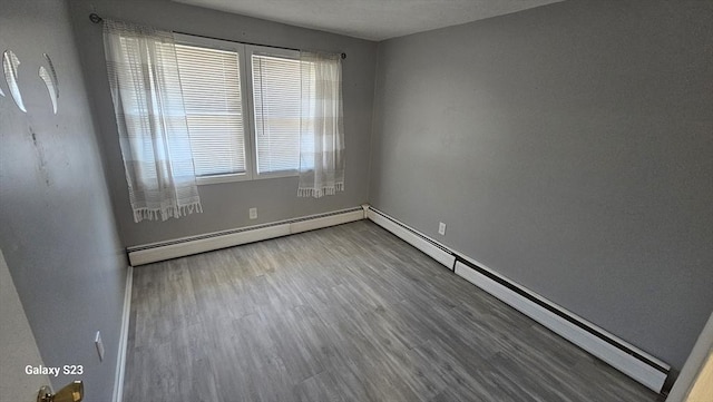 empty room featuring a baseboard radiator, baseboards, and wood finished floors