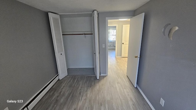 unfurnished bedroom with a closet, wood finished floors, baseboards, and a baseboard radiator