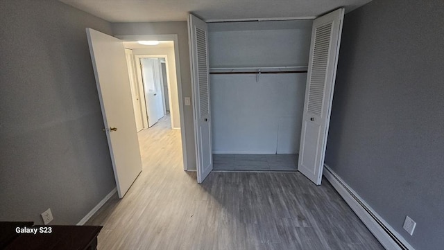 unfurnished bedroom featuring a baseboard heating unit, wood finished floors, a closet, and baseboards