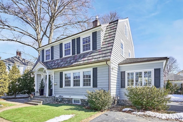 view of front of house featuring a front yard, a chimney, and a gambrel roof