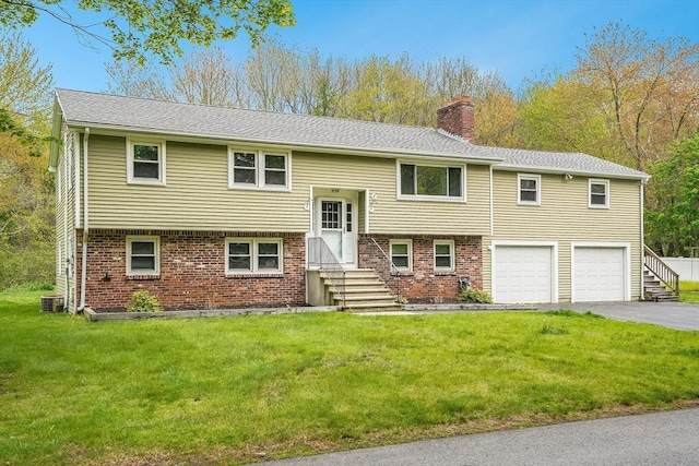 bi-level home featuring entry steps, a chimney, driveway, brick siding, and a garage