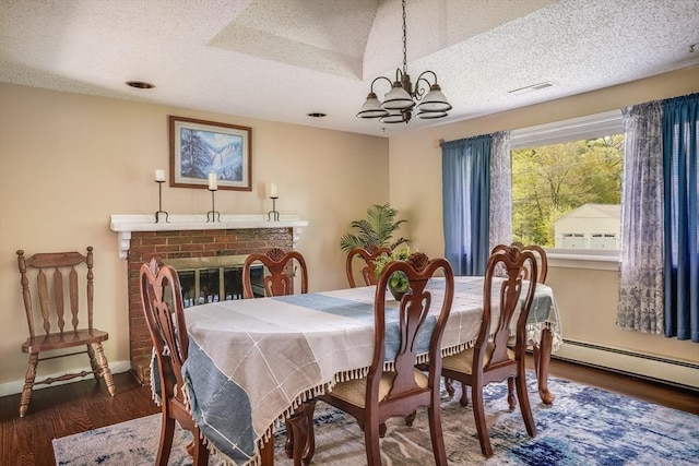 dining area with a textured ceiling, wood finished floors, a chandelier, a fireplace, and baseboards