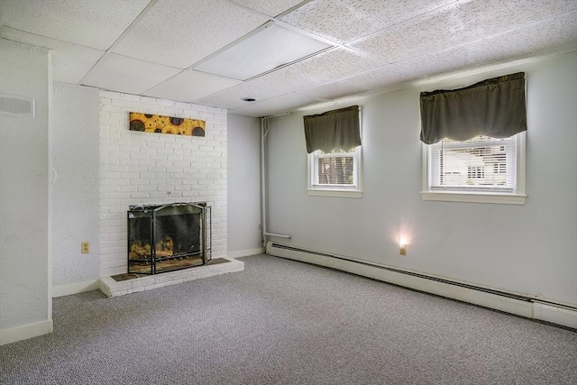 unfurnished living room featuring a baseboard heating unit, carpet, a brick fireplace, a drop ceiling, and baseboards