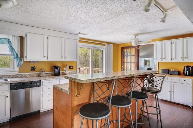 kitchen with dishwasher, dark wood-style floors, a kitchen bar, white cabinetry, and a textured ceiling
