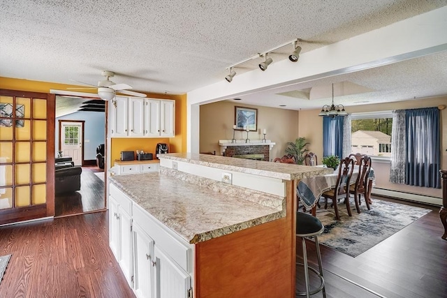 kitchen featuring a baseboard heating unit, dark wood-style flooring, a kitchen island, a textured ceiling, and light countertops