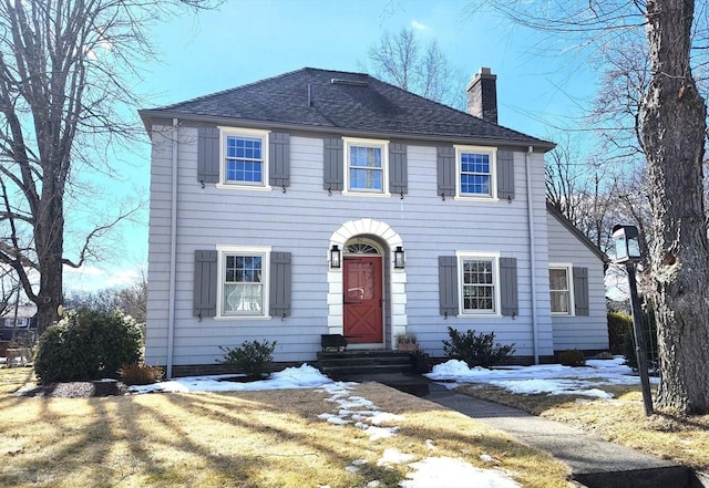 colonial inspired home featuring entry steps, a shingled roof, a chimney, and a lawn