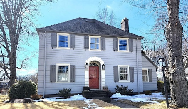 colonial house with entry steps, roof with shingles, and a chimney