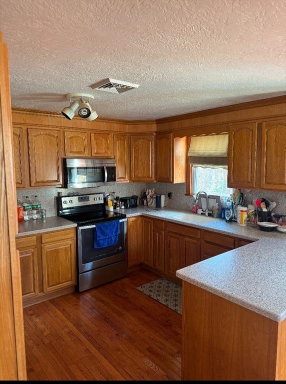 kitchen with kitchen peninsula, sink, a textured ceiling, dark hardwood / wood-style floors, and stainless steel appliances