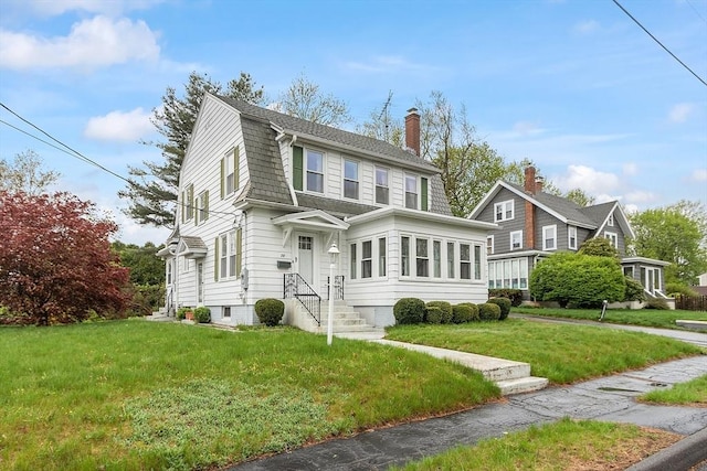 colonial inspired home featuring a chimney, a gambrel roof, and a front yard