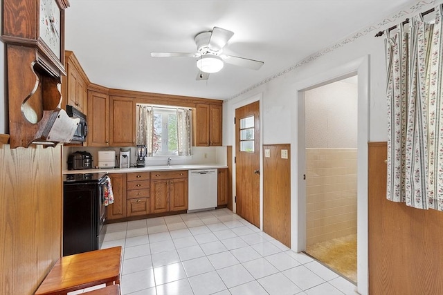 kitchen featuring black appliances, light countertops, wainscoting, ceiling fan, and a sink