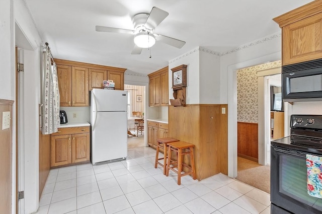 kitchen featuring black appliances, wainscoting, light countertops, a ceiling fan, and wood walls