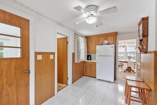 kitchen with freestanding refrigerator, a wainscoted wall, light countertops, a ceiling fan, and brown cabinets