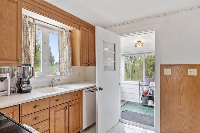 kitchen with dishwasher, a sink, brown cabinetry, light tile patterned floors, and light countertops