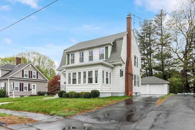 view of front of property featuring a detached garage, an outdoor structure, a front lawn, and a chimney