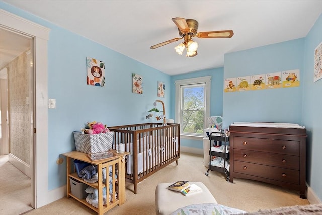 bedroom with carpet, baseboards, a ceiling fan, and a crib