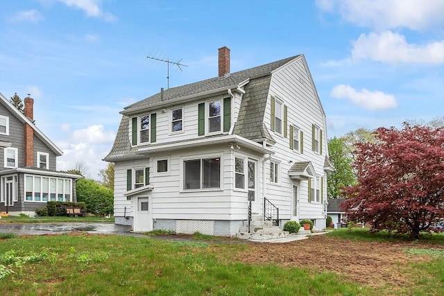 view of side of property with entry steps, a chimney, a gambrel roof, and a lawn