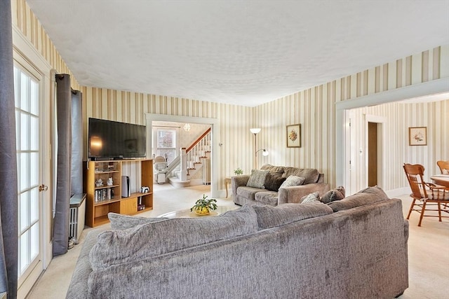 living area featuring wallpapered walls, light colored carpet, stairs, and a textured ceiling