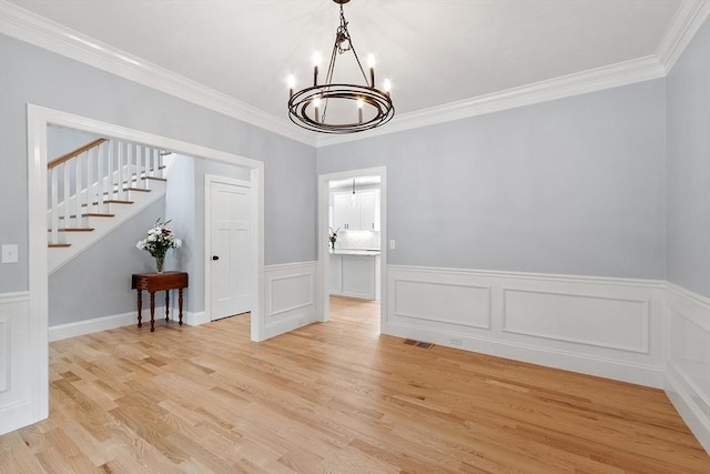 192 Tahattawan, Littleton, MA 01460 - unfurnished dining area with a chandelier, light wood-style floors, ornamental molding, stairway, and a wainscoted wall