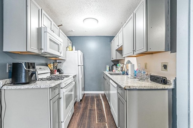 kitchen featuring dark wood-type flooring, light countertops, gray cabinets, white appliances, and a sink