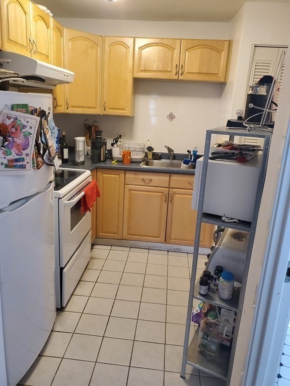 kitchen with white appliances, under cabinet range hood, light tile patterned floors, dark countertops, and a sink