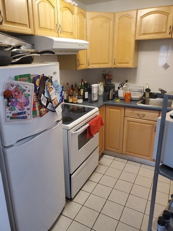 kitchen with white appliances, light tile patterned floors, light brown cabinets, dark countertops, and a sink