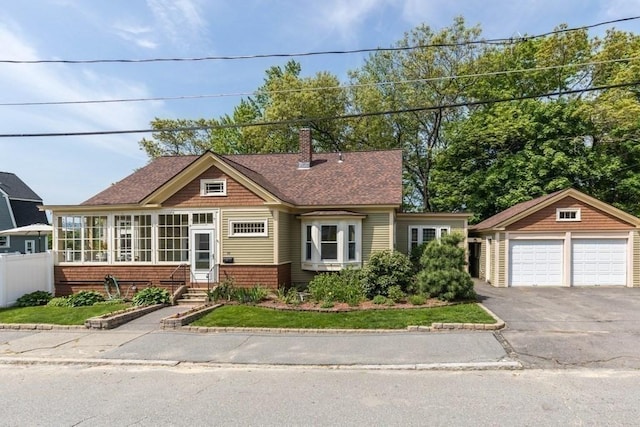 view of front facade with an outbuilding, a detached garage, fence, a sunroom, and a chimney