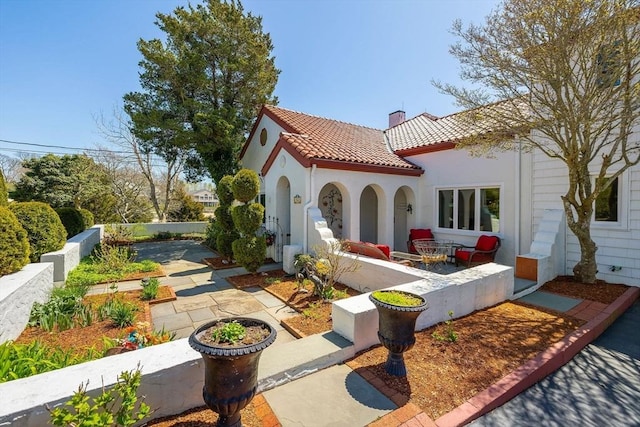 rear view of property featuring a chimney, stucco siding, a tile roof, and a patio
