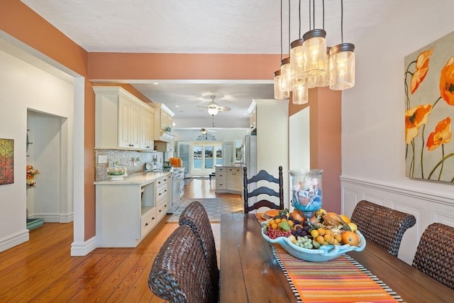 dining space with baseboards, light wood-style floors, and ceiling fan with notable chandelier
