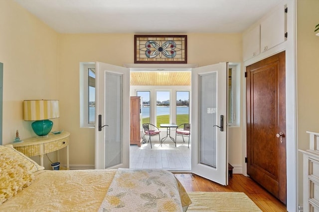 bedroom featuring a water view, baseboards, light wood finished floors, and access to exterior