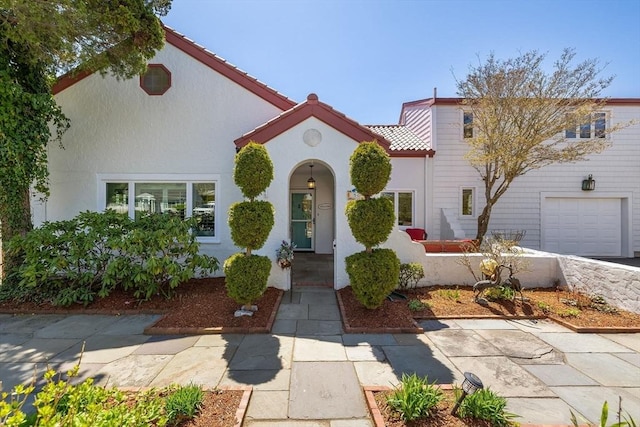 mediterranean / spanish house featuring stucco siding, a tile roof, and a garage