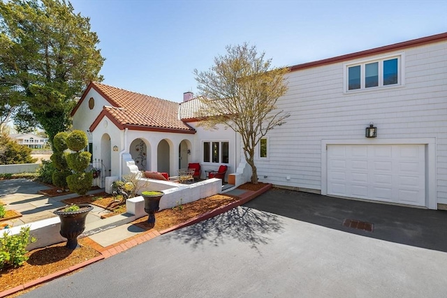 view of front of house featuring driveway, a tile roof, a garage, stucco siding, and a chimney