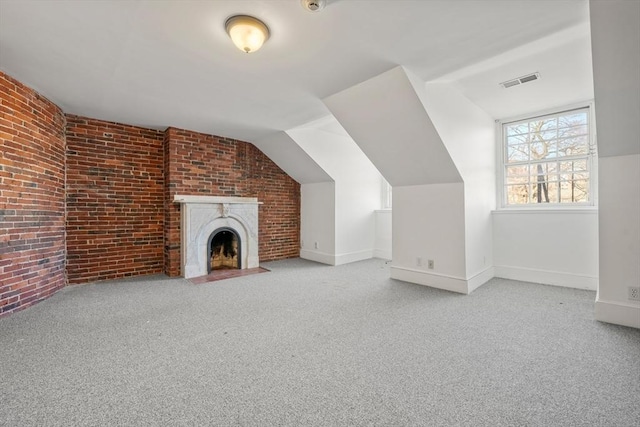 unfurnished living room featuring visible vents, brick wall, carpet, a fireplace with flush hearth, and lofted ceiling