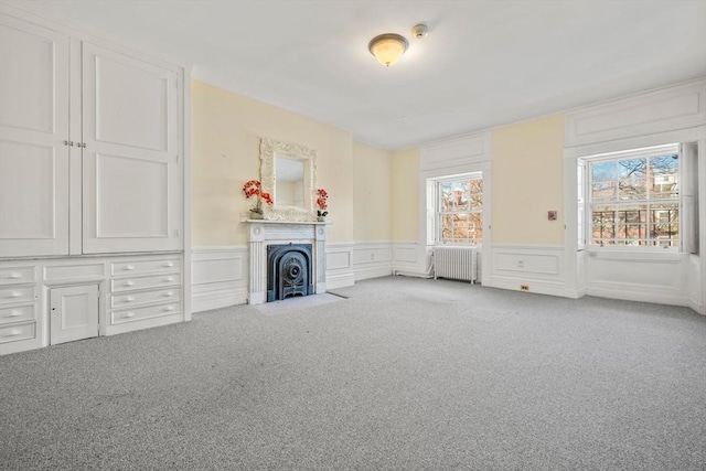 unfurnished living room with a fireplace with flush hearth, wainscoting, radiator heating unit, and carpet floors