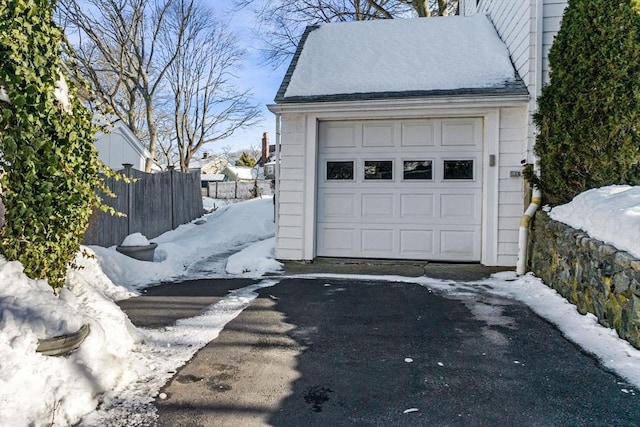 snow covered garage with aphalt driveway and fence