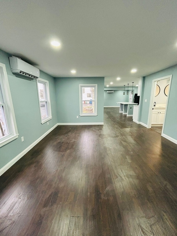 unfurnished living room with a wealth of natural light, dark wood-type flooring, and a wall mounted air conditioner