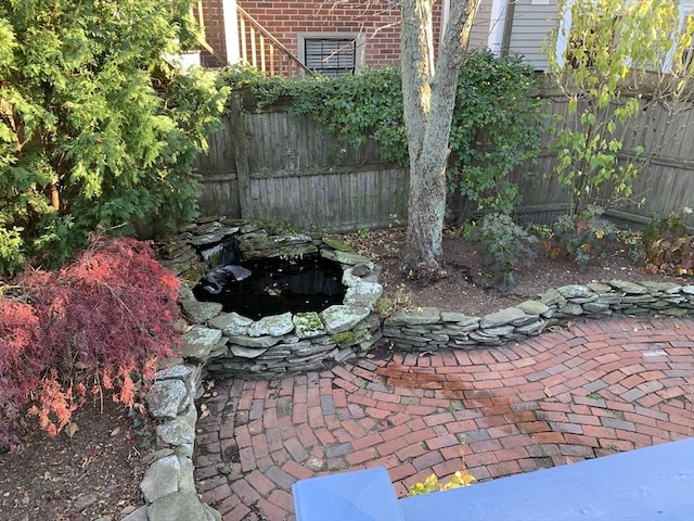 view of yard featuring a garden pond, an outdoor fire pit, fence, and a patio