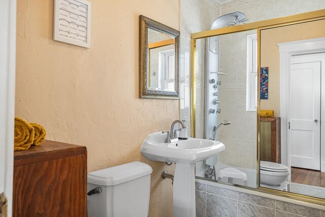 full bathroom featuring toilet, tiled shower / bath combo, and a textured wall