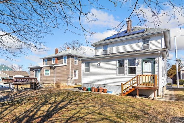 rear view of house featuring solar panels, a chimney, and a lawn