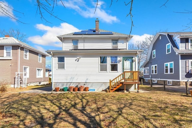 back of property featuring solar panels, a yard, and a chimney