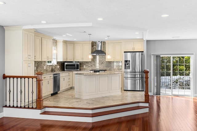 kitchen featuring light wood-type flooring, decorative backsplash, stainless steel appliances, wall chimney exhaust hood, and cream cabinets