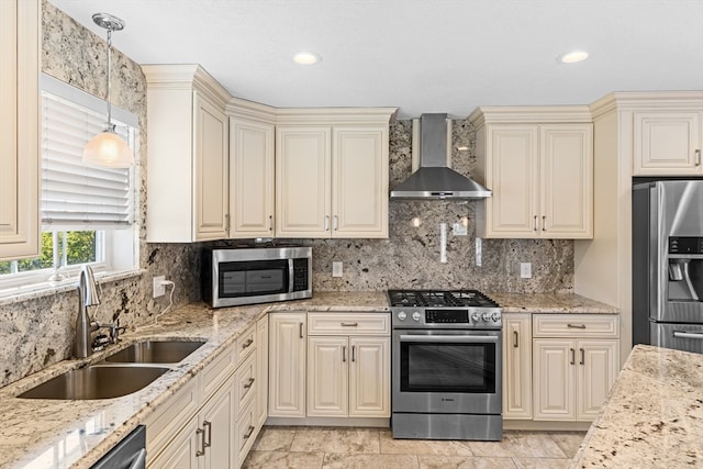 kitchen featuring hanging light fixtures, sink, wall chimney exhaust hood, cream cabinetry, and appliances with stainless steel finishes