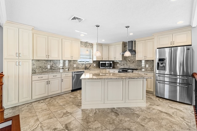 kitchen with hanging light fixtures, a kitchen island, wall chimney range hood, stainless steel appliances, and light stone countertops