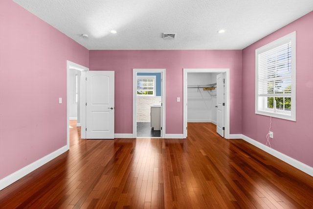 unfurnished bedroom featuring dark wood-type flooring, a spacious closet, a closet, and a textured ceiling